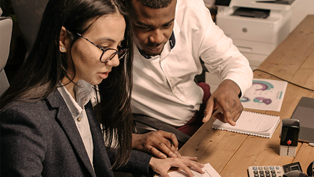 Two people looking over paperwork with a calculator on the table