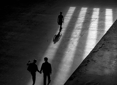 Three people walking inside a building casting shadows