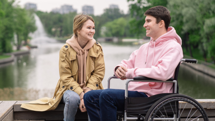 A man in a wheelchair and an able-bodied woman chat by a river